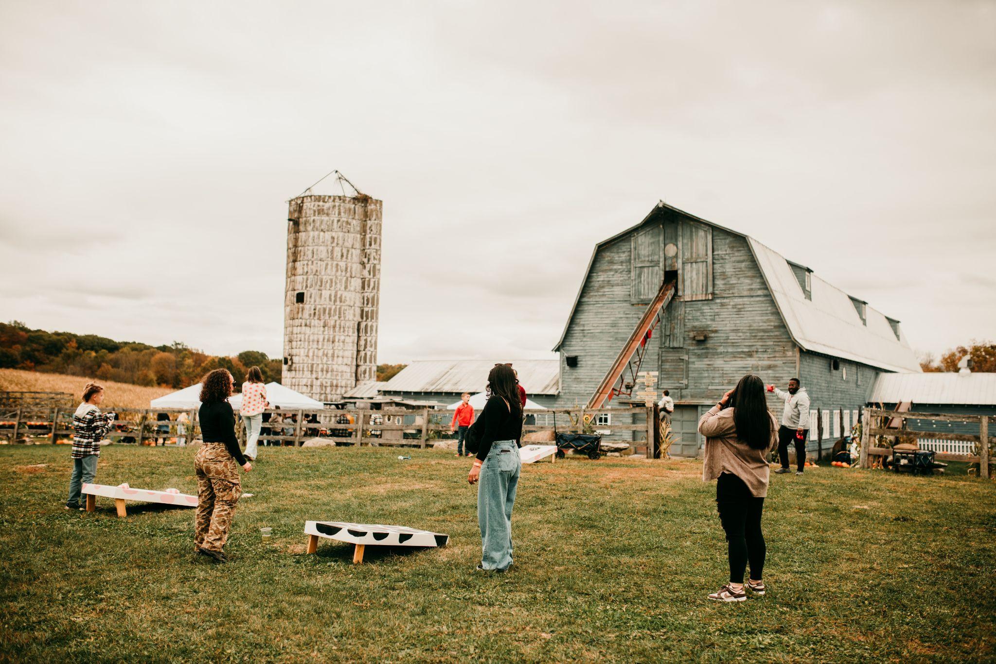 Guests playing corn hole on the lawn with the barn and silo behind
