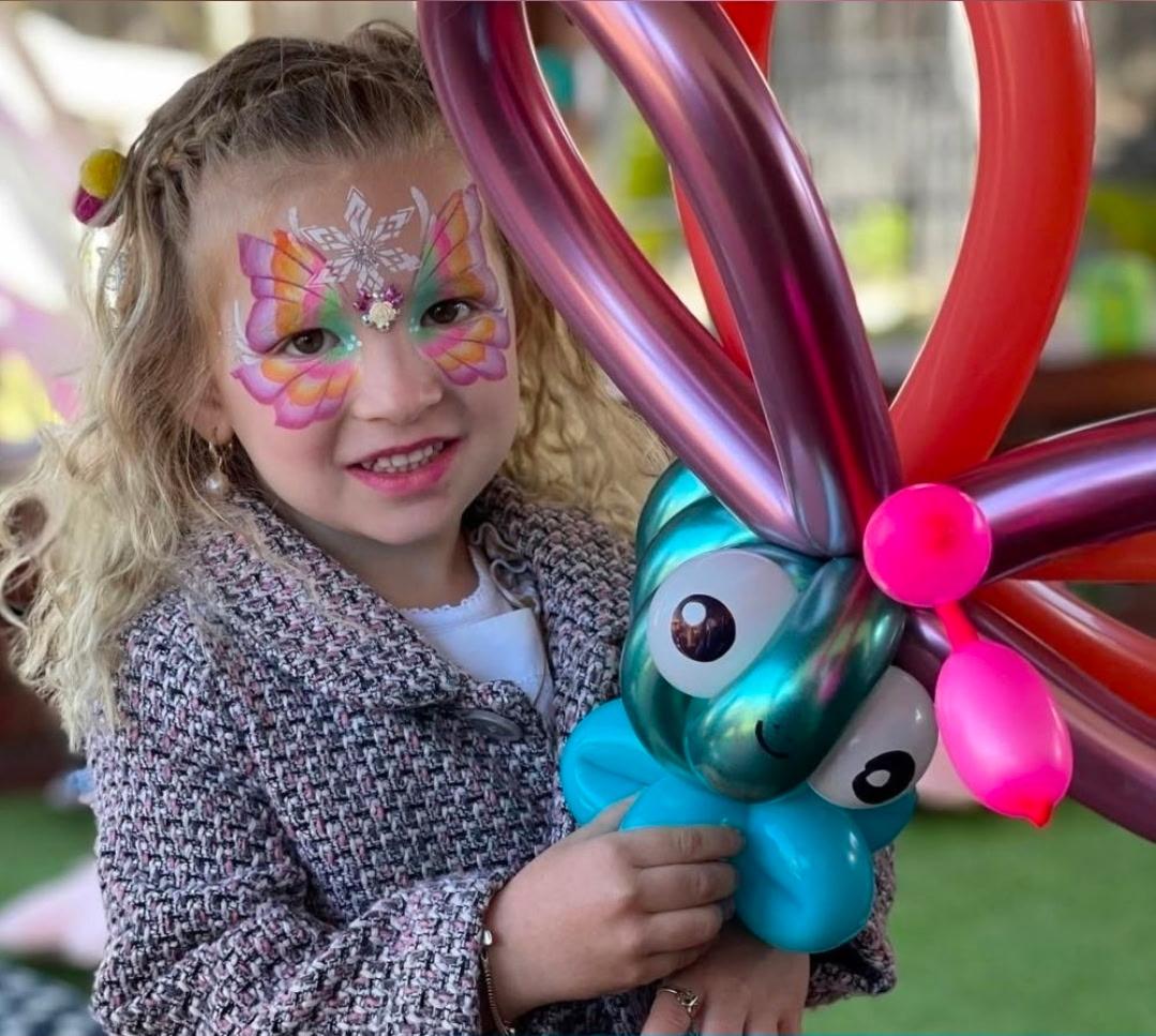 A girl with butterfly face paint holding a balloon animal